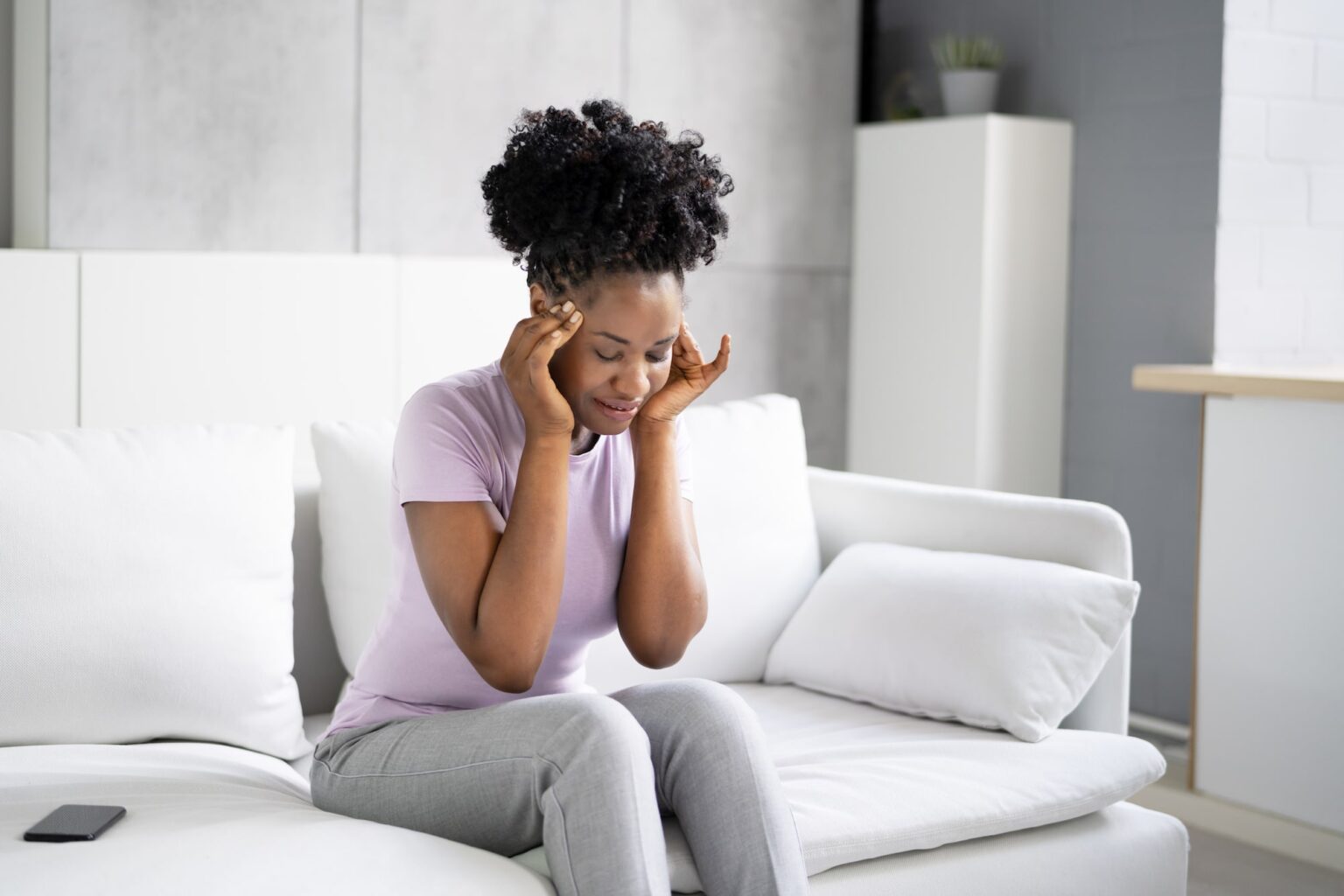Woman on the couch holding her temples lightly with her hands while experiencing a bppv spell
